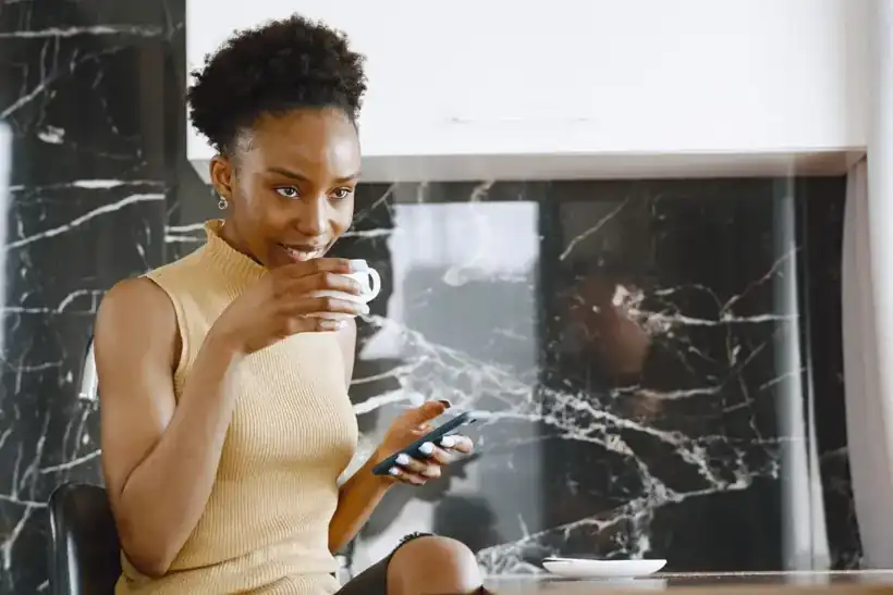 A woman sipping her morning coffee while checking her phone at home