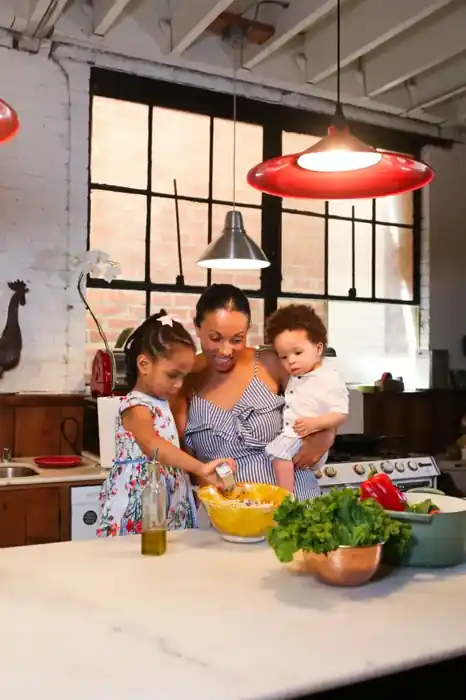 A mom making a fresh salad in the kitchen with her two young children