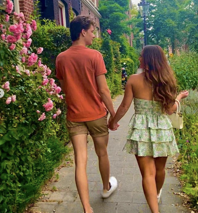 Liev and his wife walking hand in hand along a flower-lined path