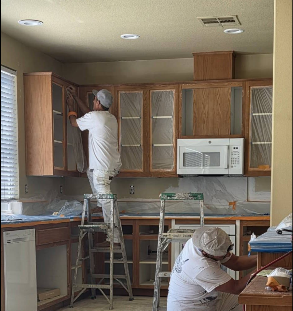 Two Upper Room painters prepping and masking kitchen cabinets before refinishing.