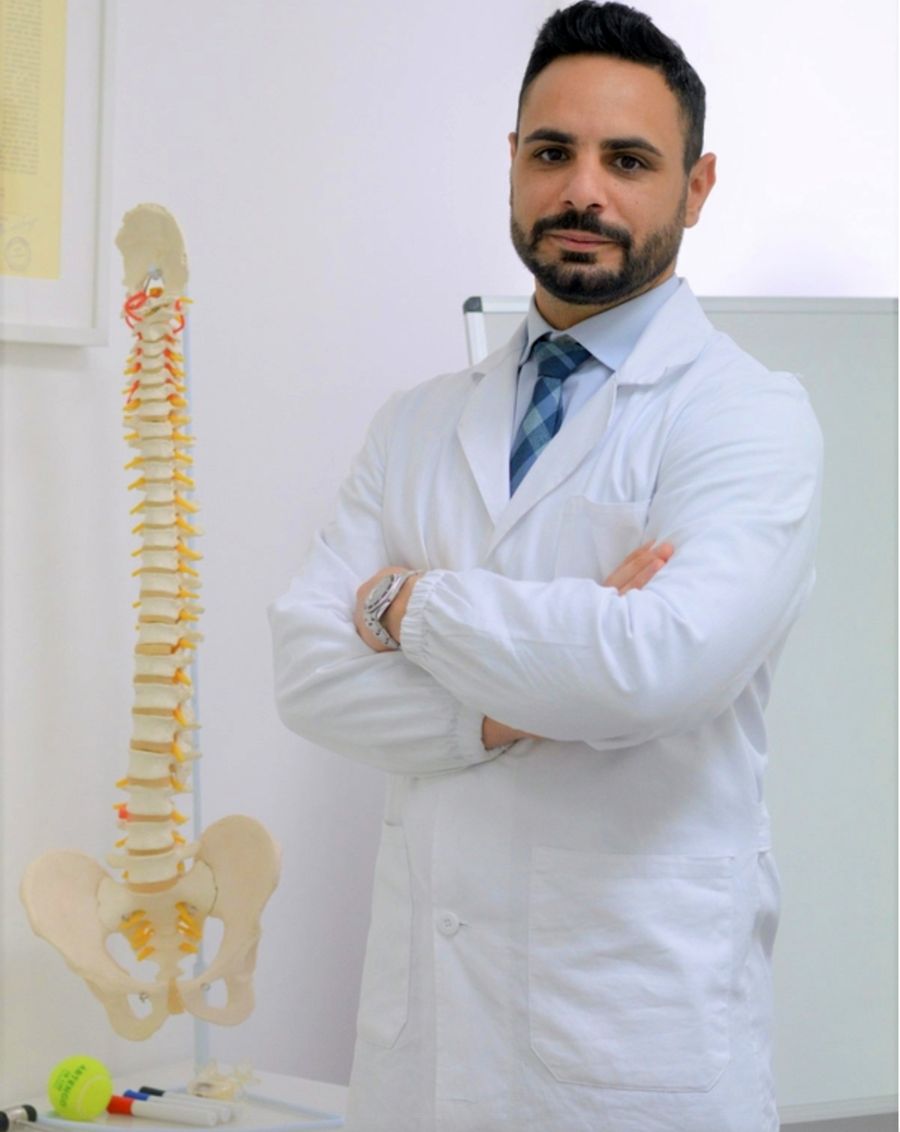 Alessio Collalti, osteopata e fisioterapista, in camice accanto a un modello di colonna vertebrale