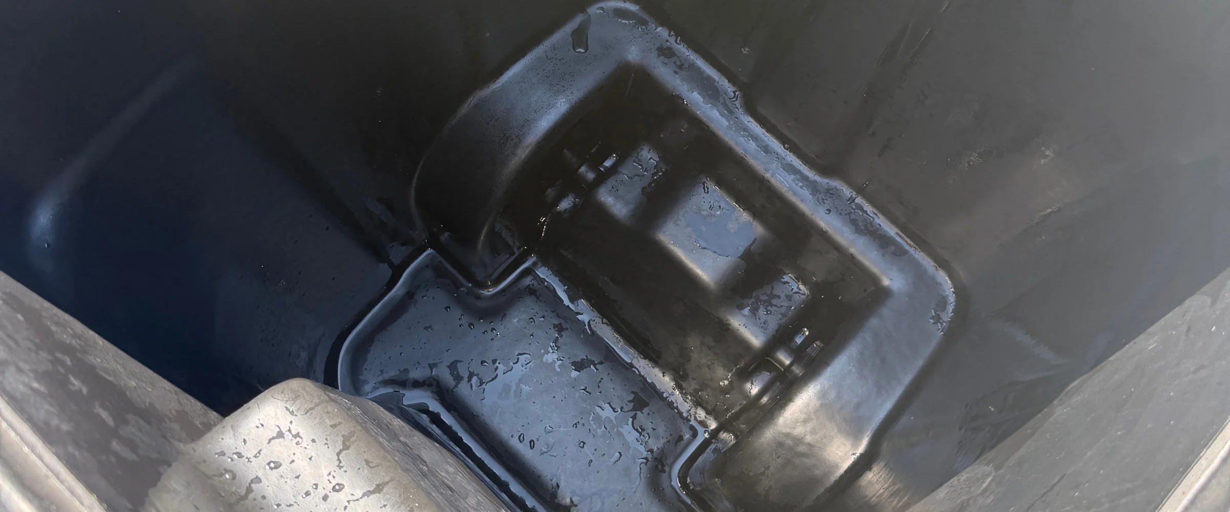 A close-up view looking down into a dark plastic container with water gathered on its textured bottom.