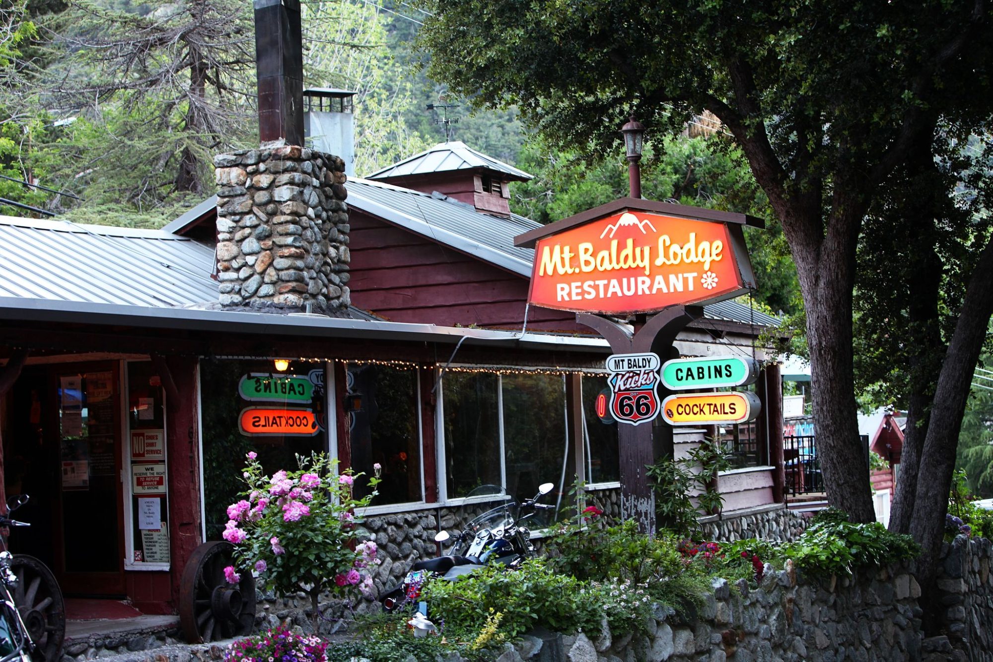 The front of the Mt Baldy Lodge with its red restaurant sign, stone chimney and pines