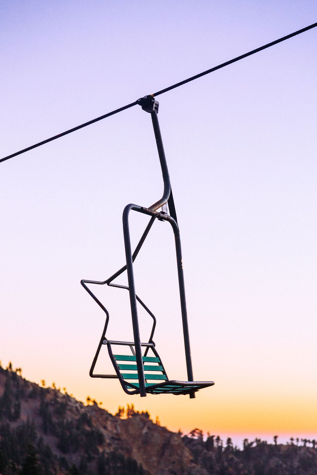 An empty chairlift chair against a pastel sunset sky