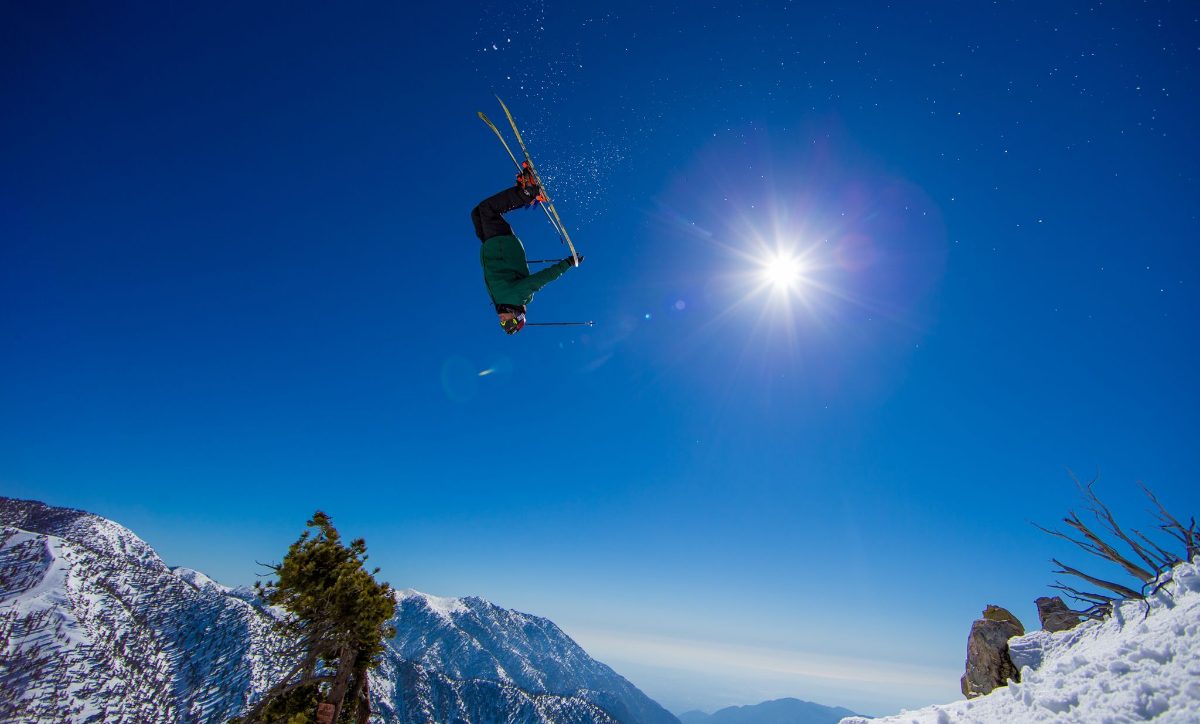 A skier in the air against the sun and snowy peaks