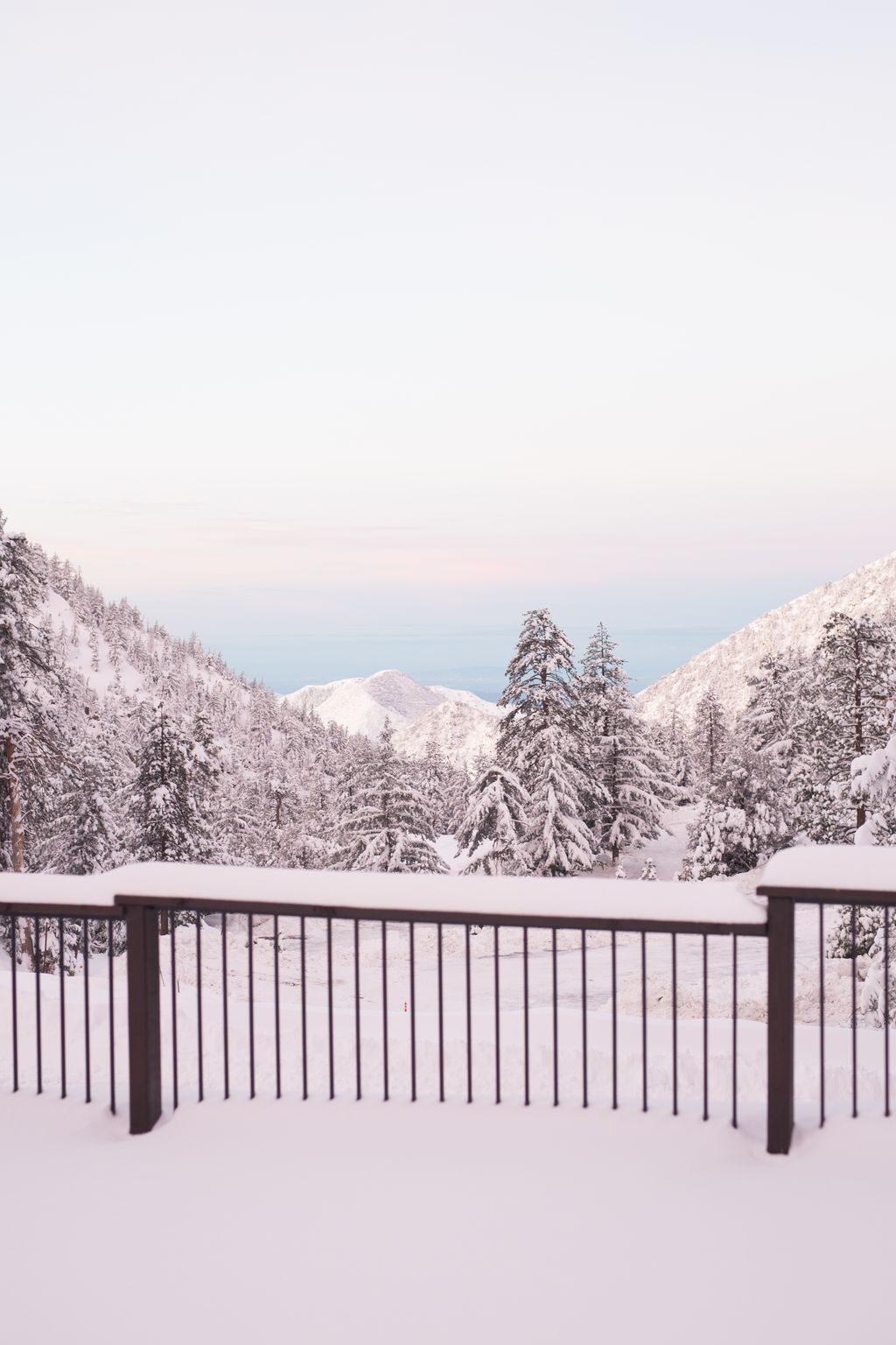Fresh snow on a deck rail with pink dusk light over the mountains