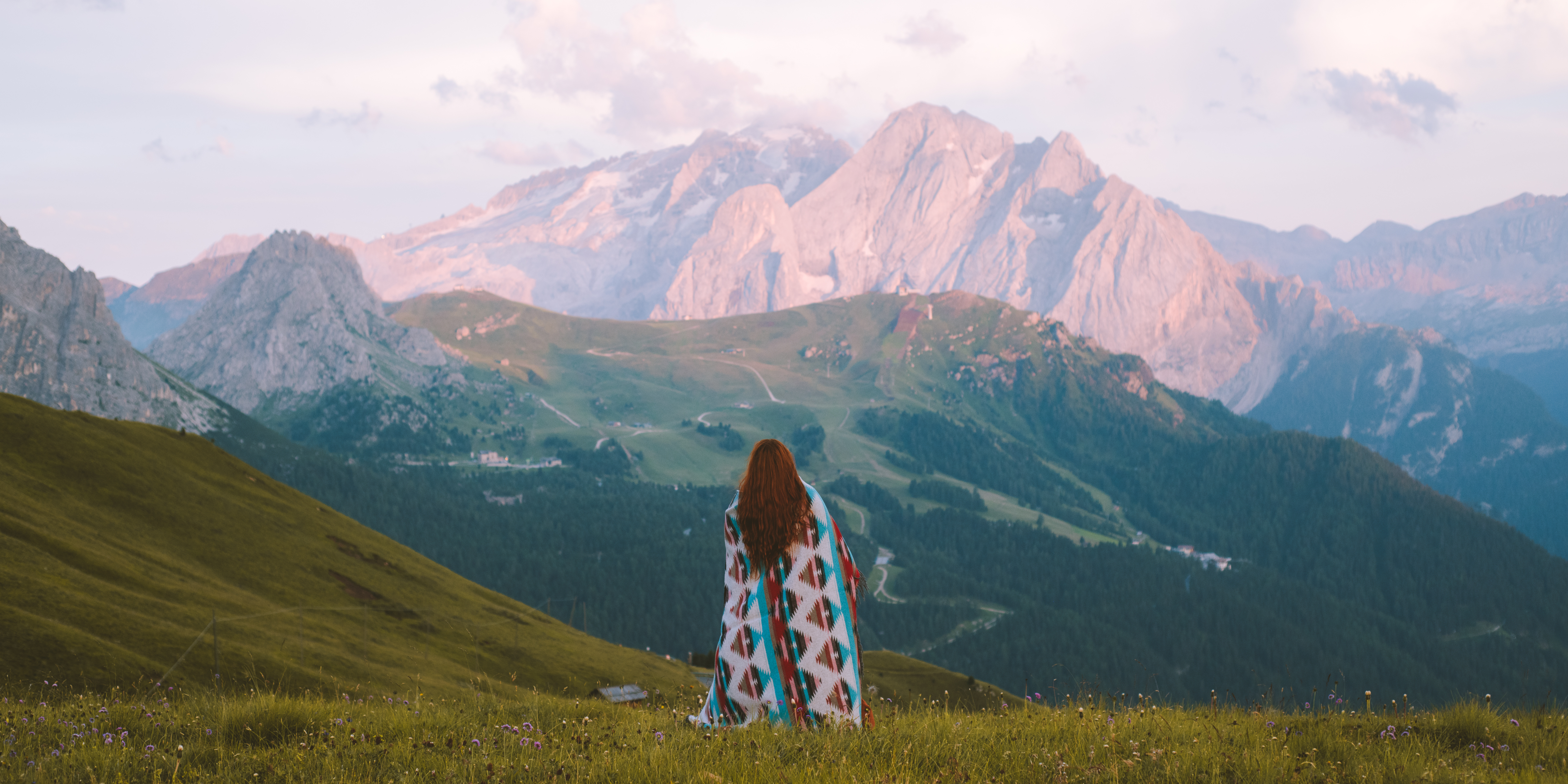 Woman wrapped in blanket facing mountains