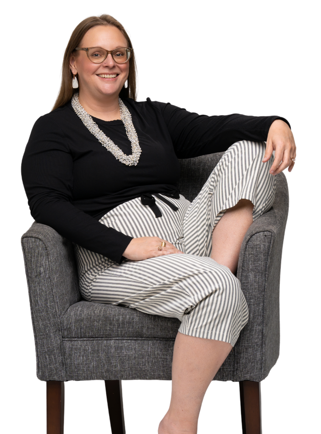 Tara sitting in a gray armchair, smiling, one arm resting on the chair back