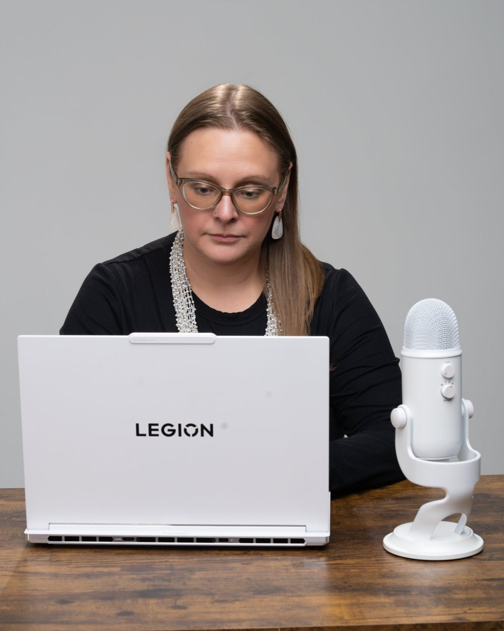 Tara working at her laptop with a white microphone on the desk beside her