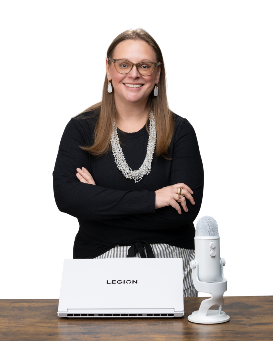 Tara smiling at her desk with a laptop and a microphone, arms crossed