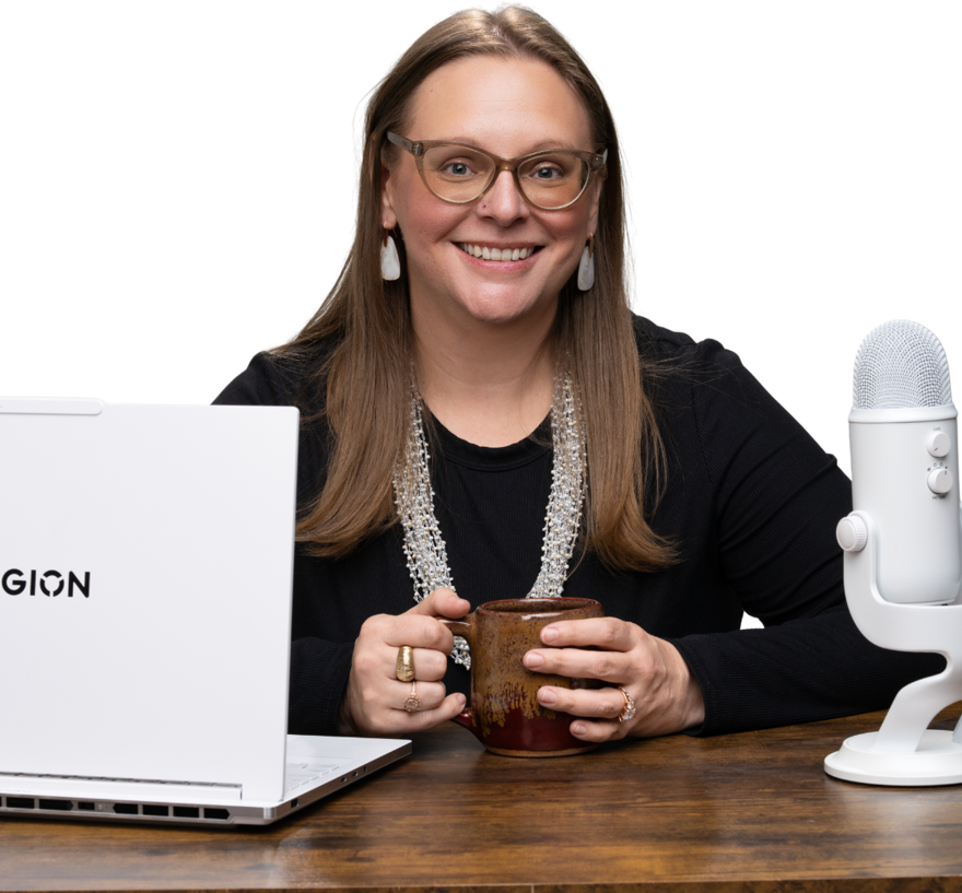 Tara smiling at her desk with a mug in her hands, a laptop on one side and a microphone on the other