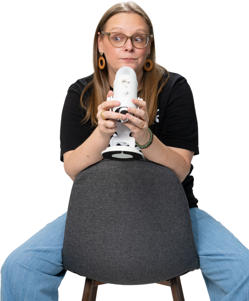Tara sitting backwards on a chair, holding a white microphone and glancing to the side