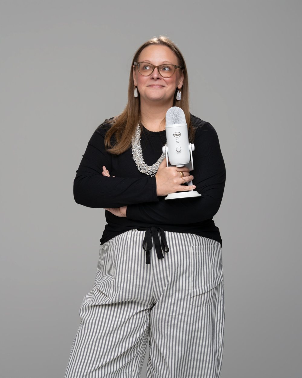 Tara with arms crossed, holding a white microphone and looking off to the side