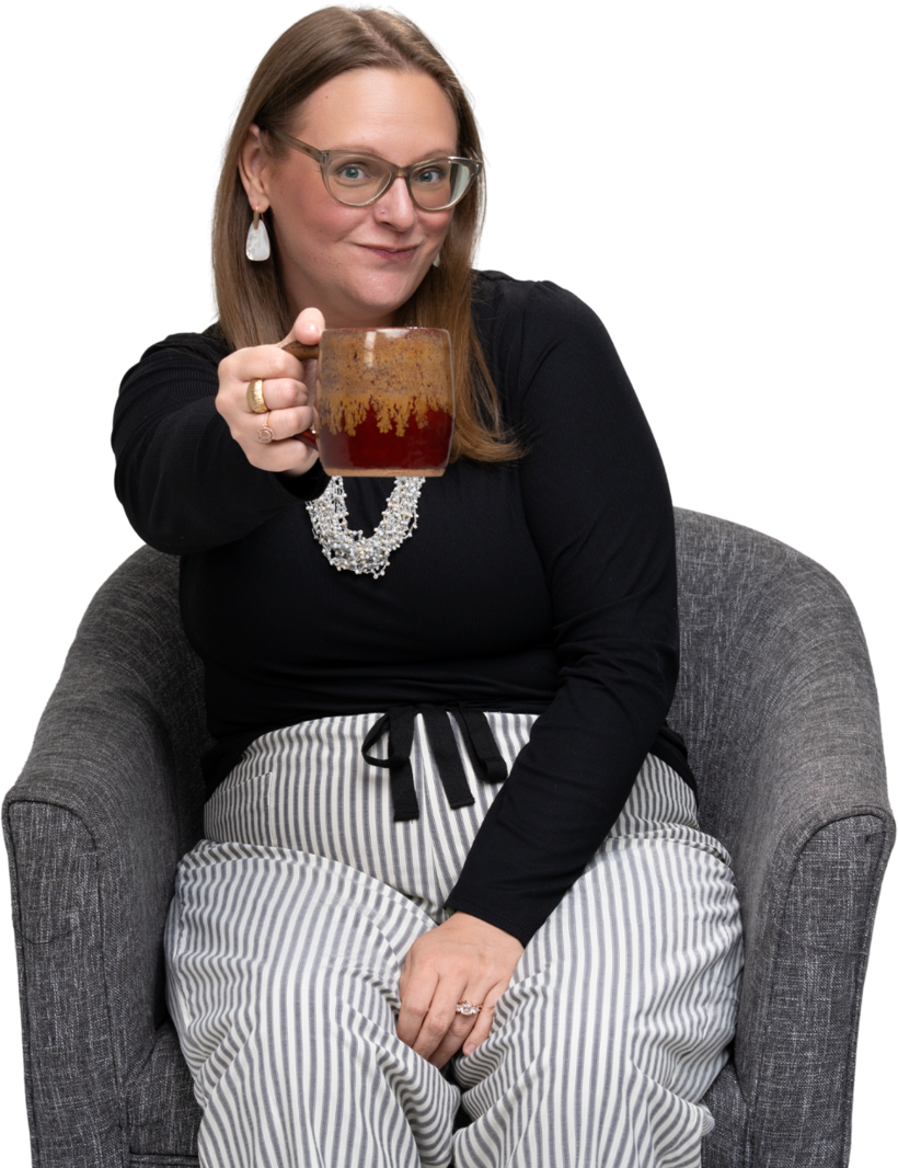 Tara sitting in an armchair, smiling and holding a mug out toward the camera