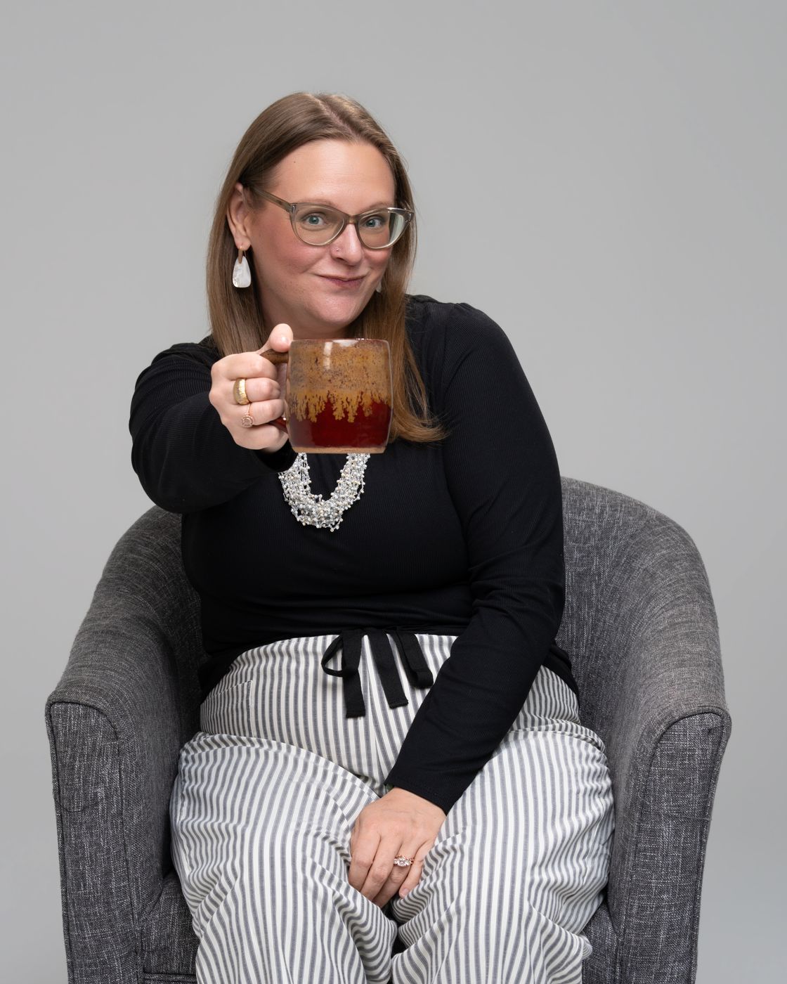 Tara in an armchair lifting a drink toward the camera