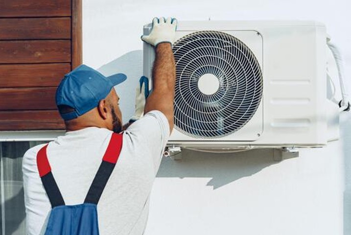 Professional HVAC installer securing an outdoor AC unit to an exterior wall