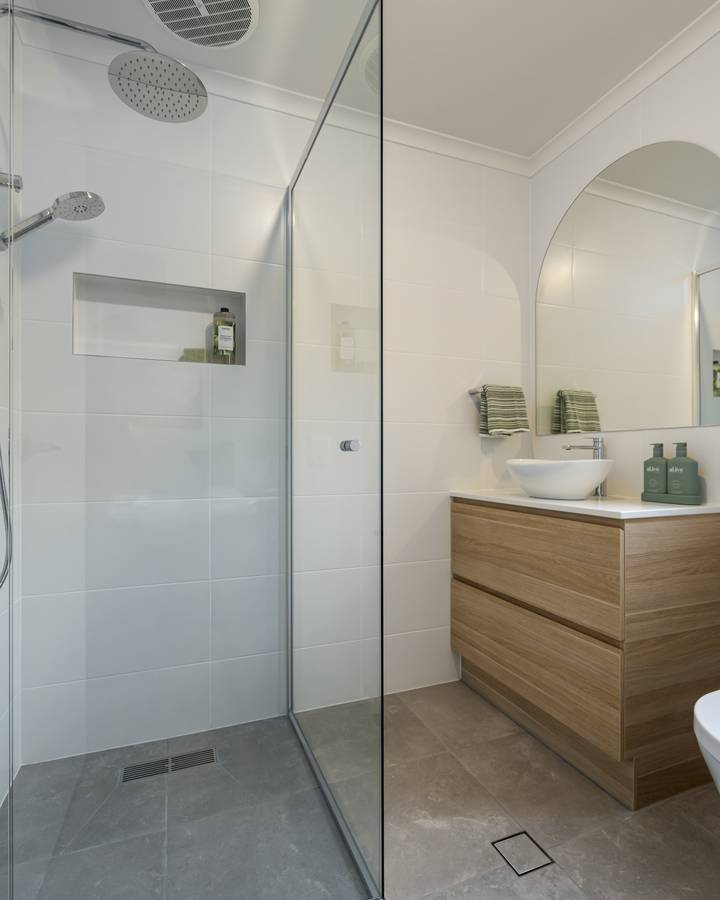 Compact bathroom: Frameless shower, arched mirror, floor-to-ceiling tiles