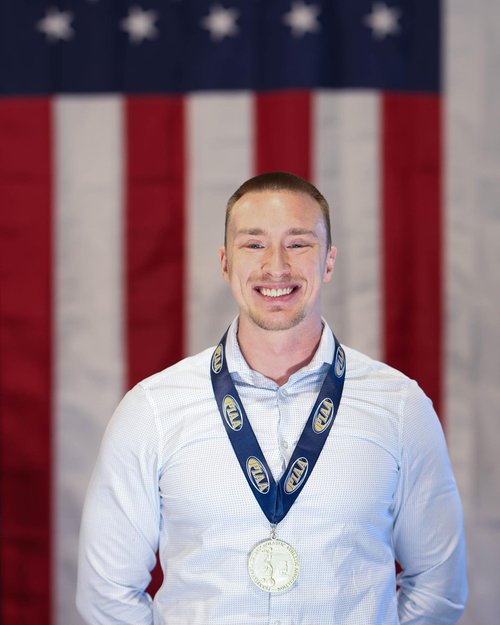 Kody Hartlaub smiling and wearing a state championship medal in front of an American flag, elite performance coach and founder of KHP Coaching
