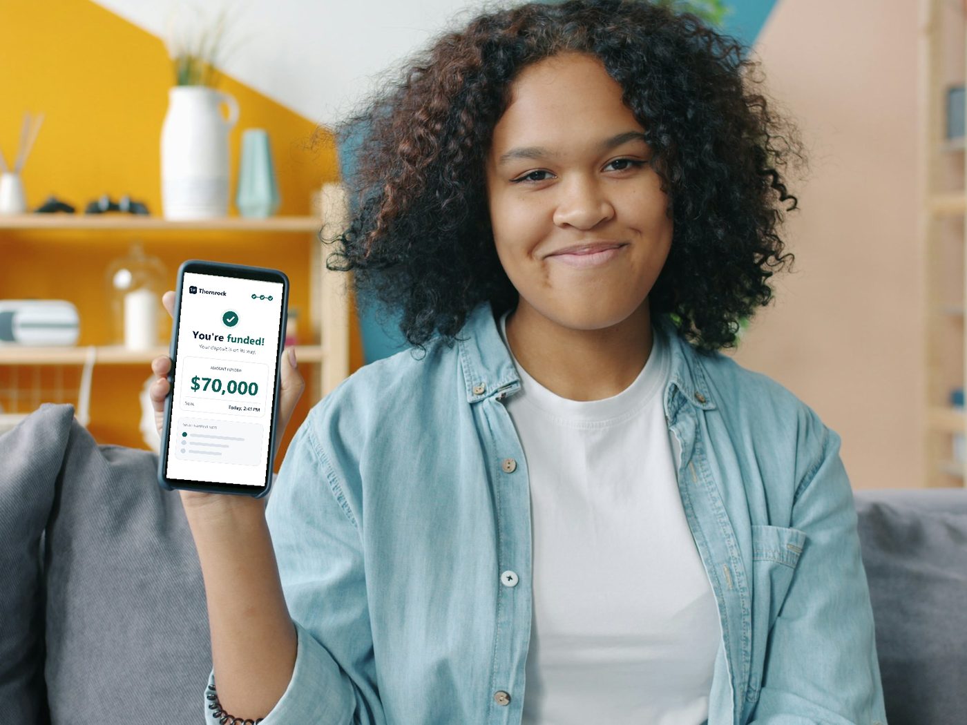 A smiling business owner holding up her phone, showing she was funded $70,000