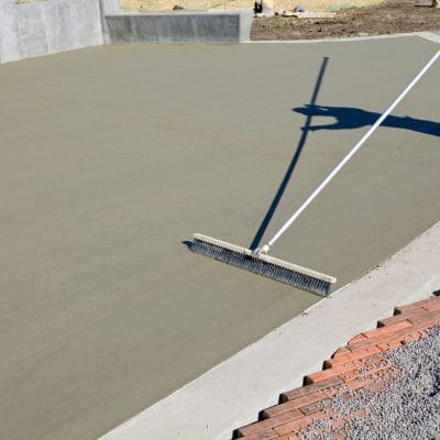 Contractor using a large broom to texture a concrete surface.