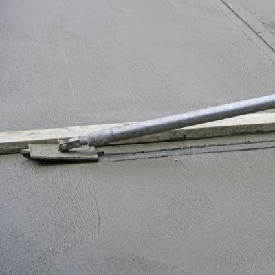 Tool being used to create control joints on freshly poured concrete sidewalk.