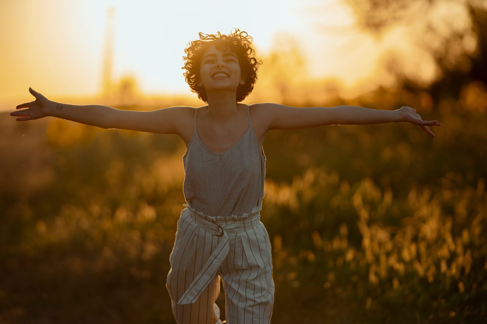A woman standing in an open field at golden hour with her arms spread wide