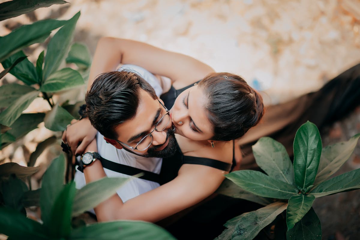 A couple sitting close together outdoors, surrounded by green foliage