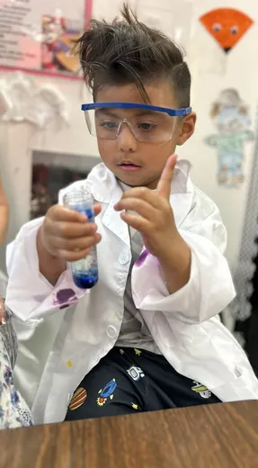 A child in a lab coat and goggles doing a science experiment