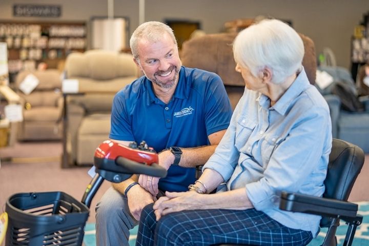 A staff member assisting a customer with a power wheelchair and mobility scooter in a medical equipment showroom. A staff member assisting a customer with a power wheelchair and mobility scooter in a medical equipment showroom.