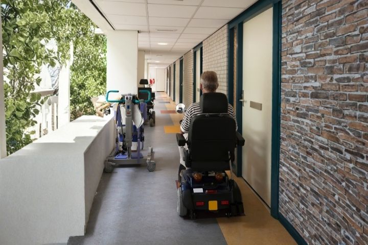A person navigating a hallway filled with various assistive devices, including a mobility scooter. A person navigating a hallway filled with various assistive devices, including a mobility scooter.