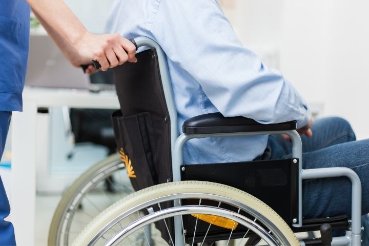 A person being assisted by a uniformed attendant in a classic model representing standard manual wheelchairs.