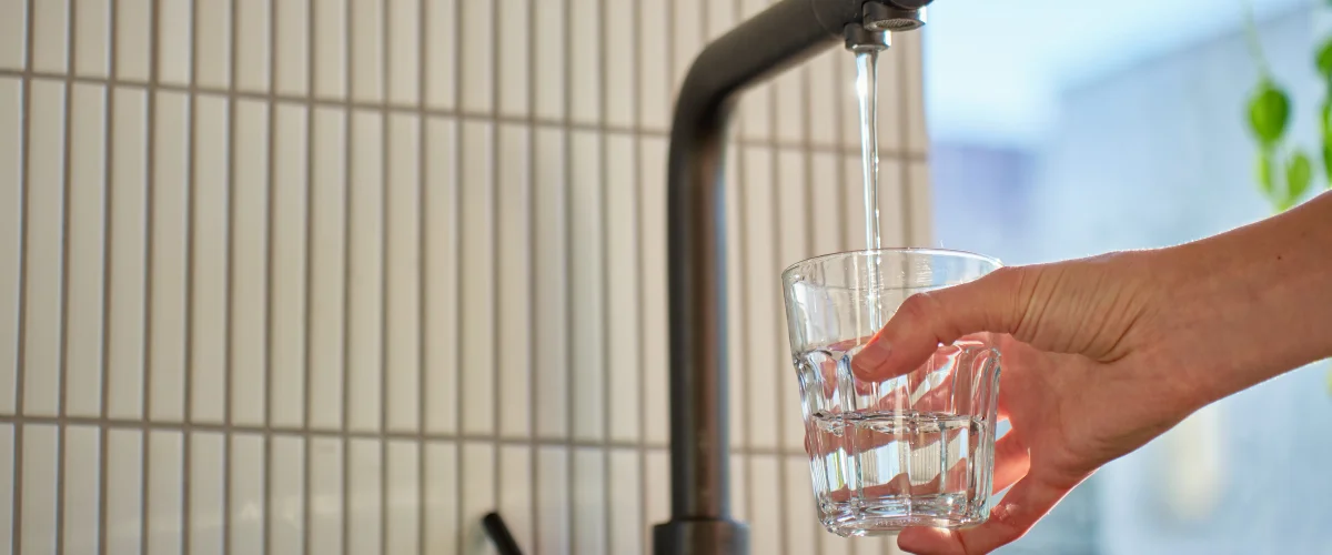 Hand filling glass with clean tap water from kitchen faucet.