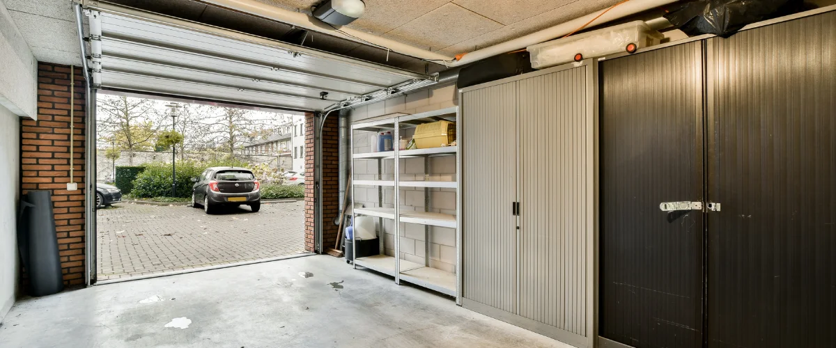 Open residential garage with shelving and car parked outside driveway.