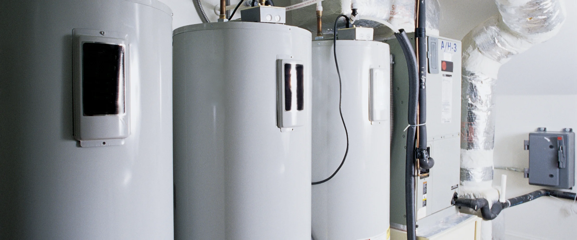 Three industrial-sized water heaters and an HVAC unit with ductwork in a utility room.
