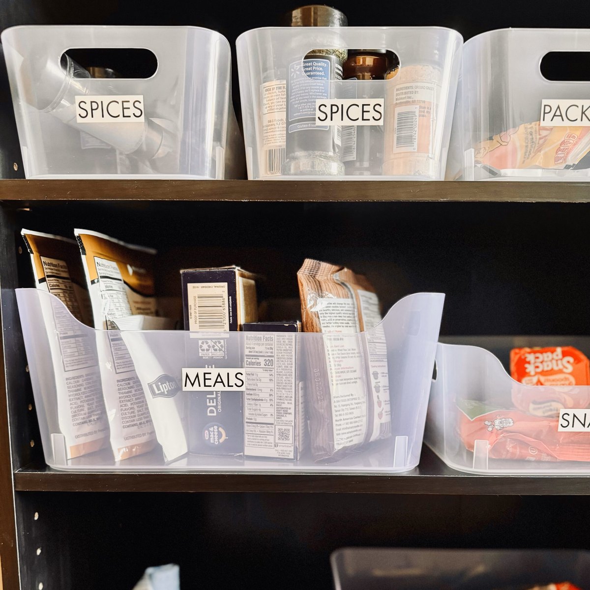 Clear bins labeled spices, meals and snacks on an open bookcase pantry Clear bins labeled spices, meals and snacks on an open bookcase pantry