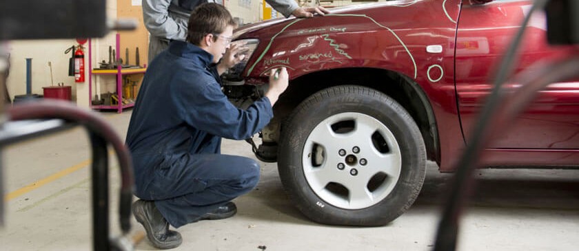 Technicians inspecting damage on the front fender of a red SUV