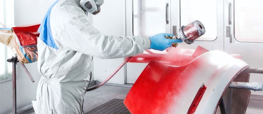 Technician spraying red paint on a car part in a spray booth