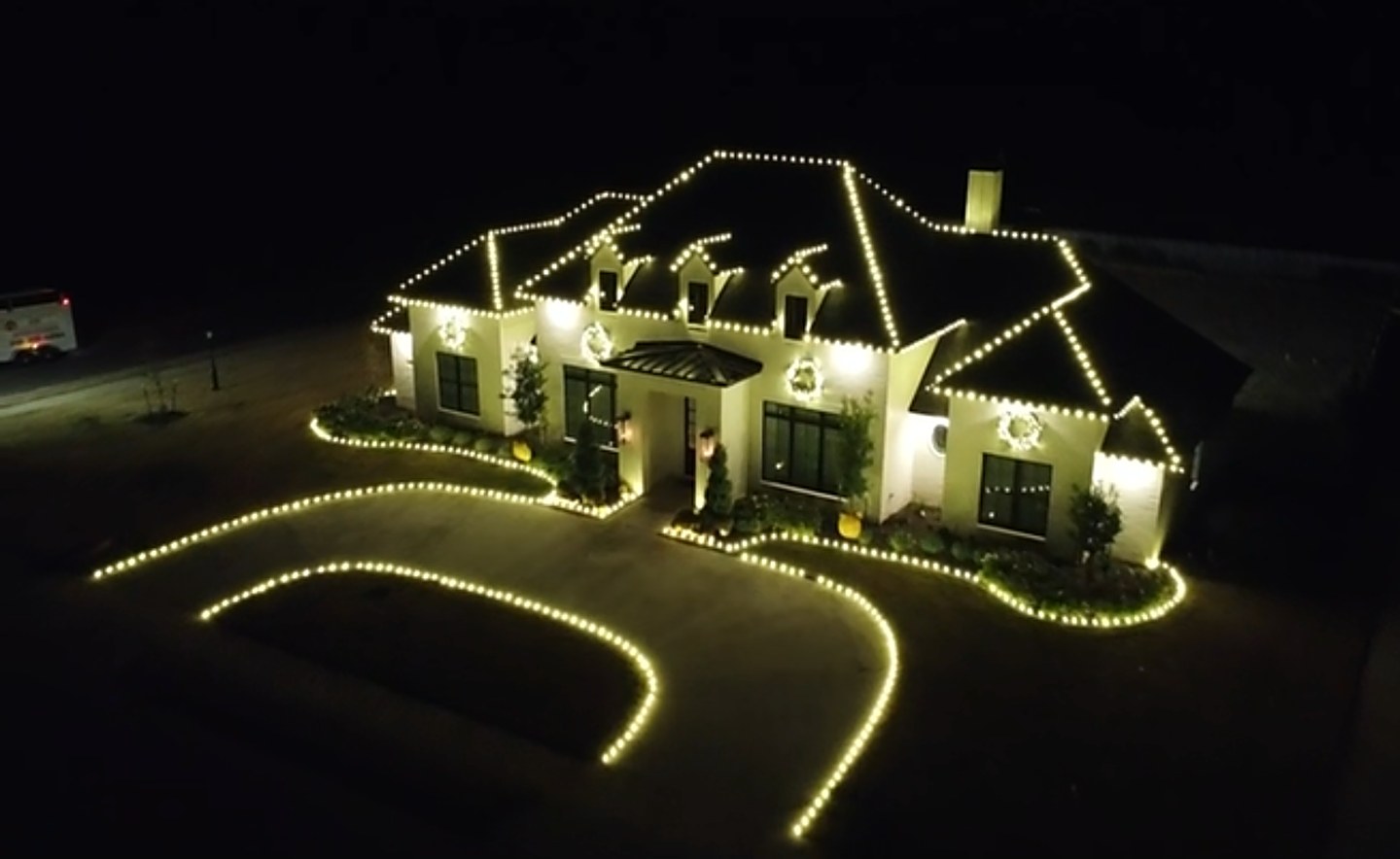 Home with warm white roofline lights, wreaths, and a lit driveway