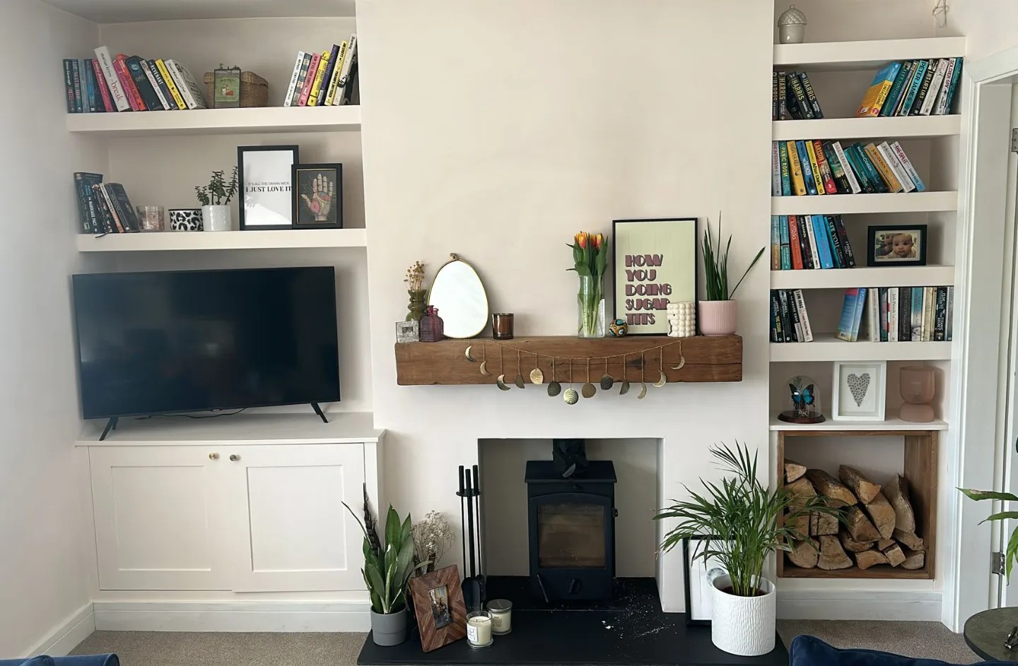 Bespoke white fitted alcove units with shelves and cabinets flanking a black wood burner fireplace, handcrafted by a West Midlands-based carpenter and joiner, showcasing custom shelving filled with books, personal mementos, and indoor plants, enhancing a cozy living room interior.