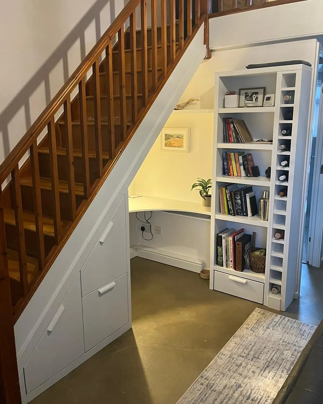 Teal-painted custom alcove cabinetry and floating shelves by a West Midlands joinery, framing a cozy fireplace stocked with firewood, with a wall-mounted TV above, and tastefully decorated with plants, photos, and books, adding a touch of personal style to a traditional UK home living room.