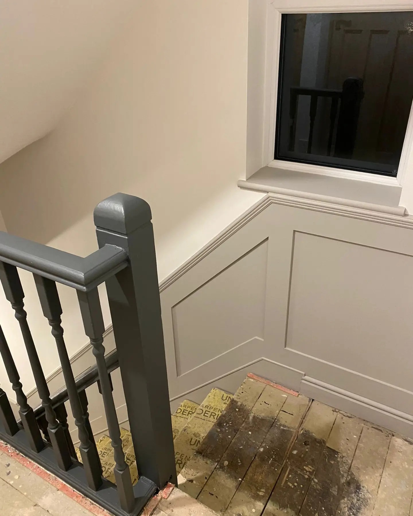 Staircase landing area featuring elegant dark grey paneling and a classic white-painted banister, part of a bespoke interior carpentry project by a West Midlands craftsman, showcasing the contrast of traditional and modern elements in a UK home during renovation.