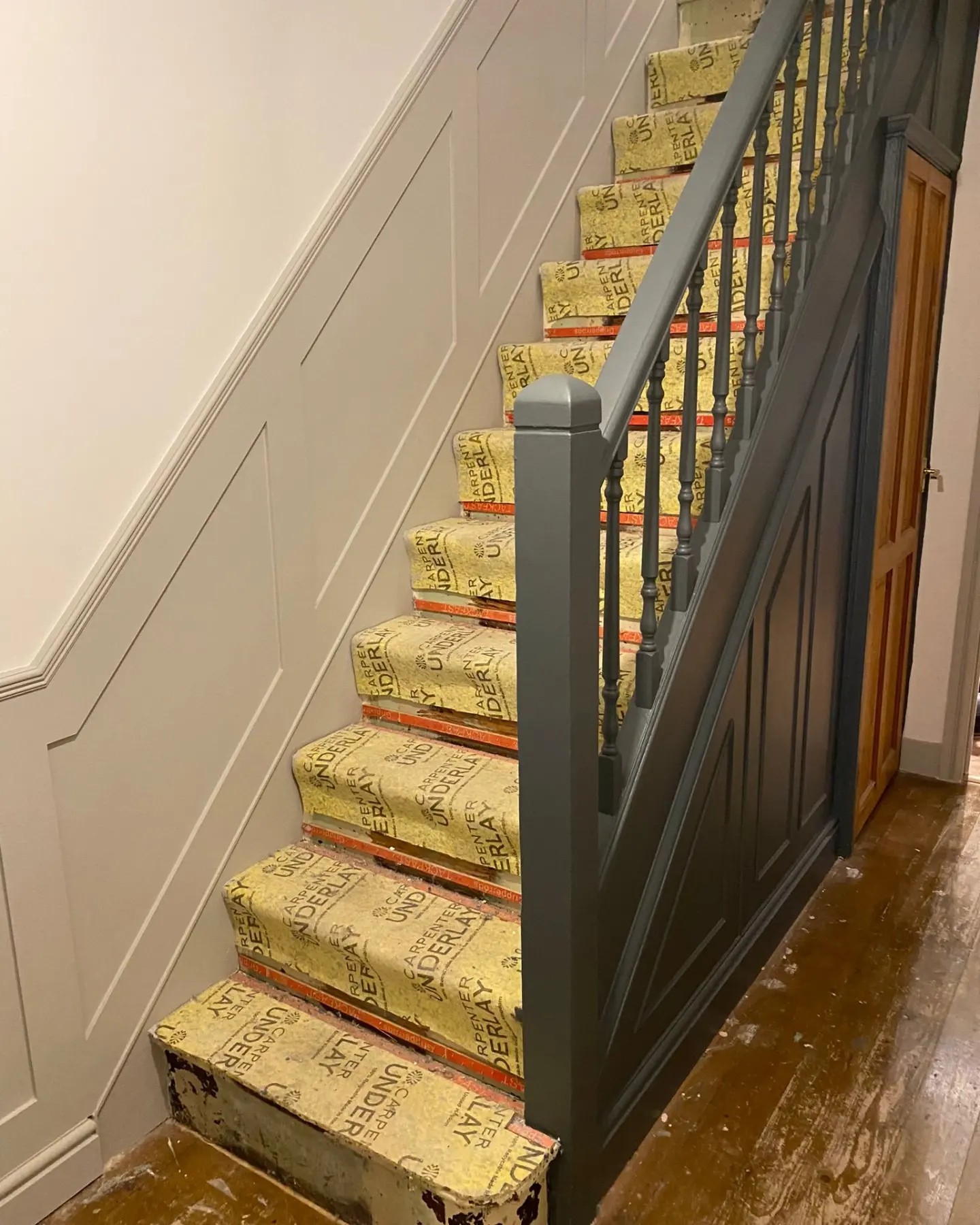 A staircase with sophisticated wall paneling in a soft grey, contrasting with the natural wood of the steps and handrail, all custom-fitted by a skilled West Midlands joiner, showcasing a blend of classic design and contemporary craftsmanship in a home undergoing stylish renovations.