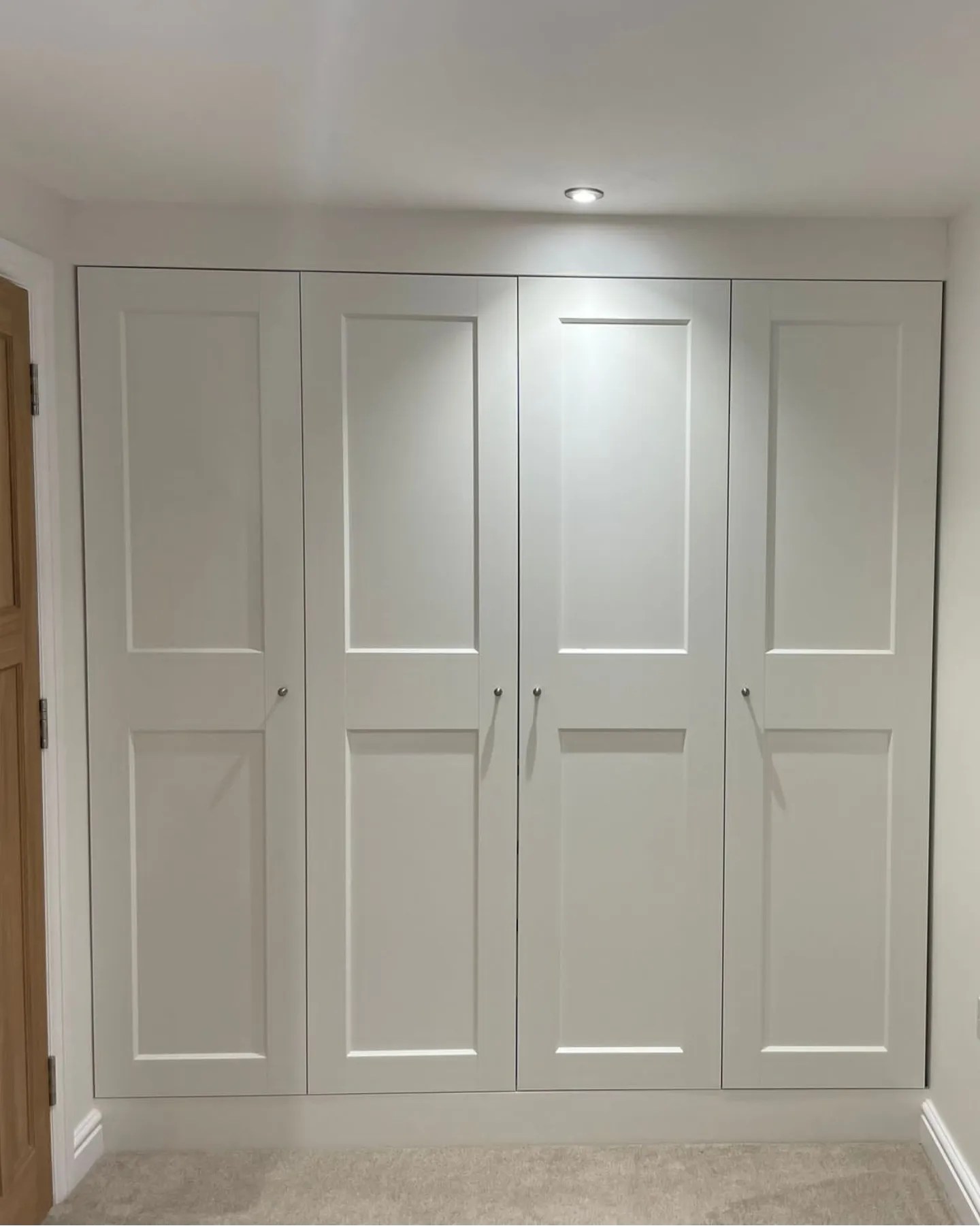 Sleek, modern white fitted wardrobes with classic panel design, custom-built to maximize storage in a West Midlands home, featuring streamlined handles and soft lighting that enhances the tranquil and tidy atmosphere of the room.