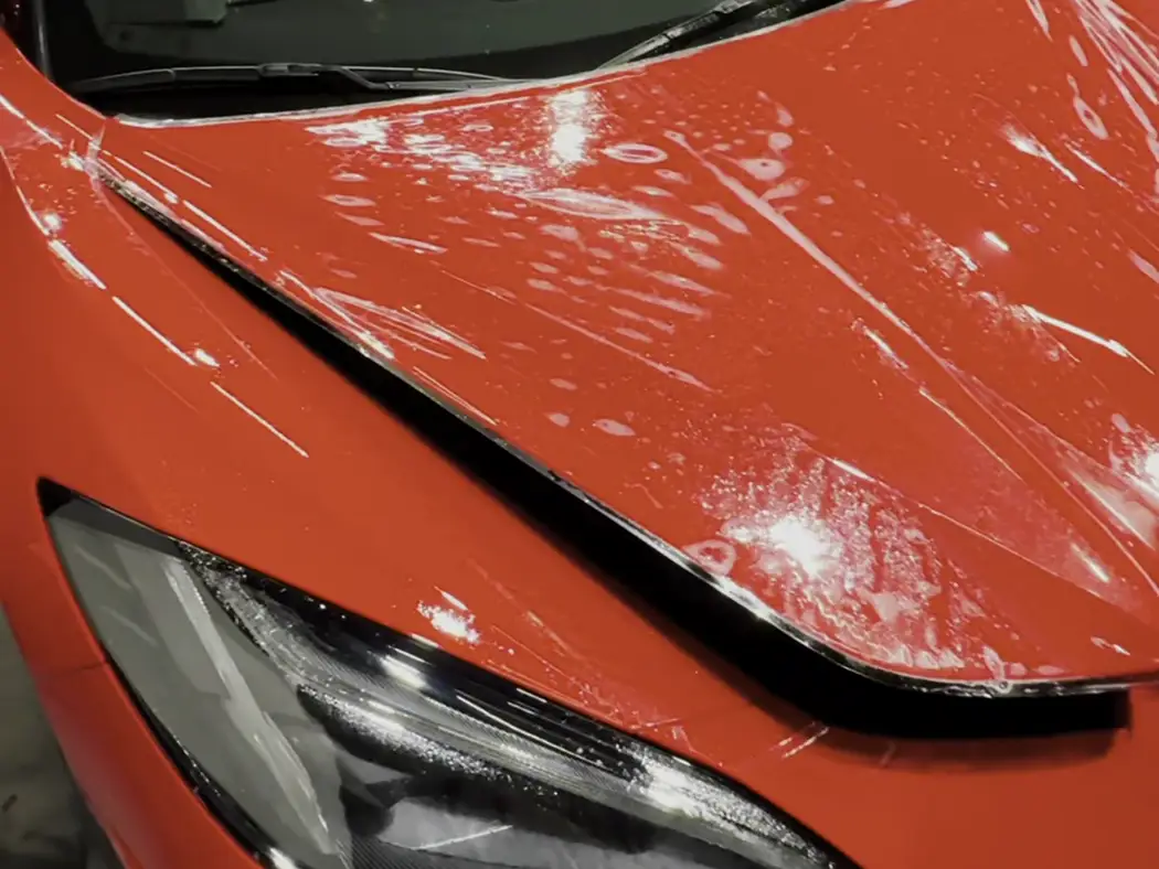 Clear film freshly laid across an orange Corvette hood and front end