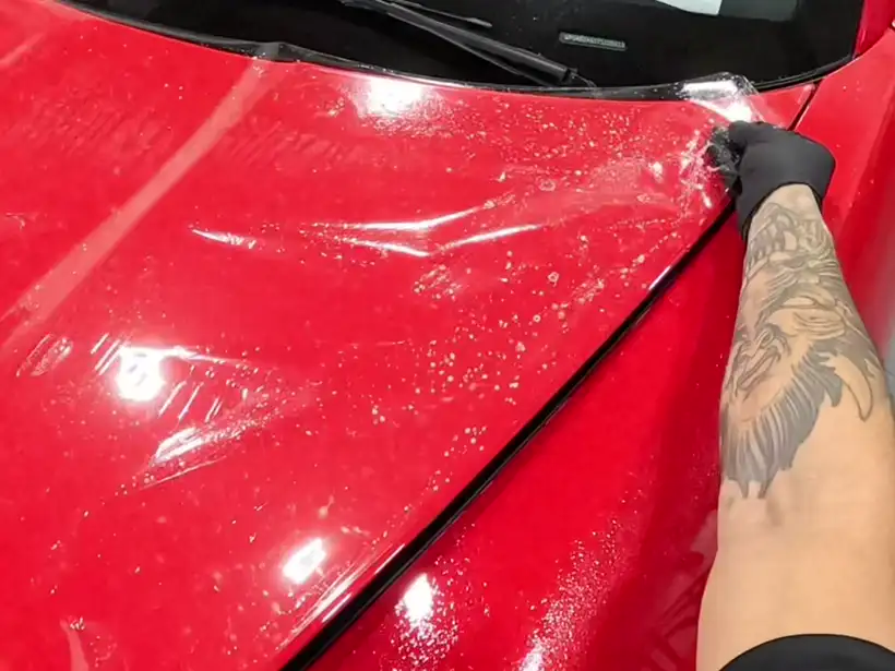 Wet clear film being set on the red hood of a Porsche