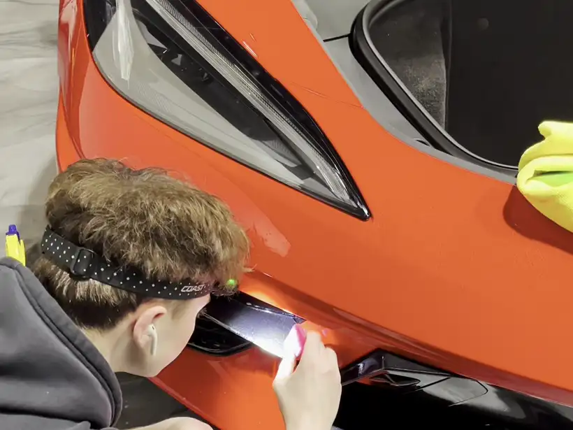 Installer working film at the front bumper of an orange Corvette