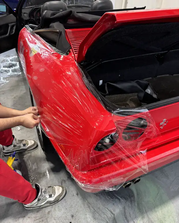 Clear film pulled over the rear quarter of a red Ferrari in the AutoCore bay