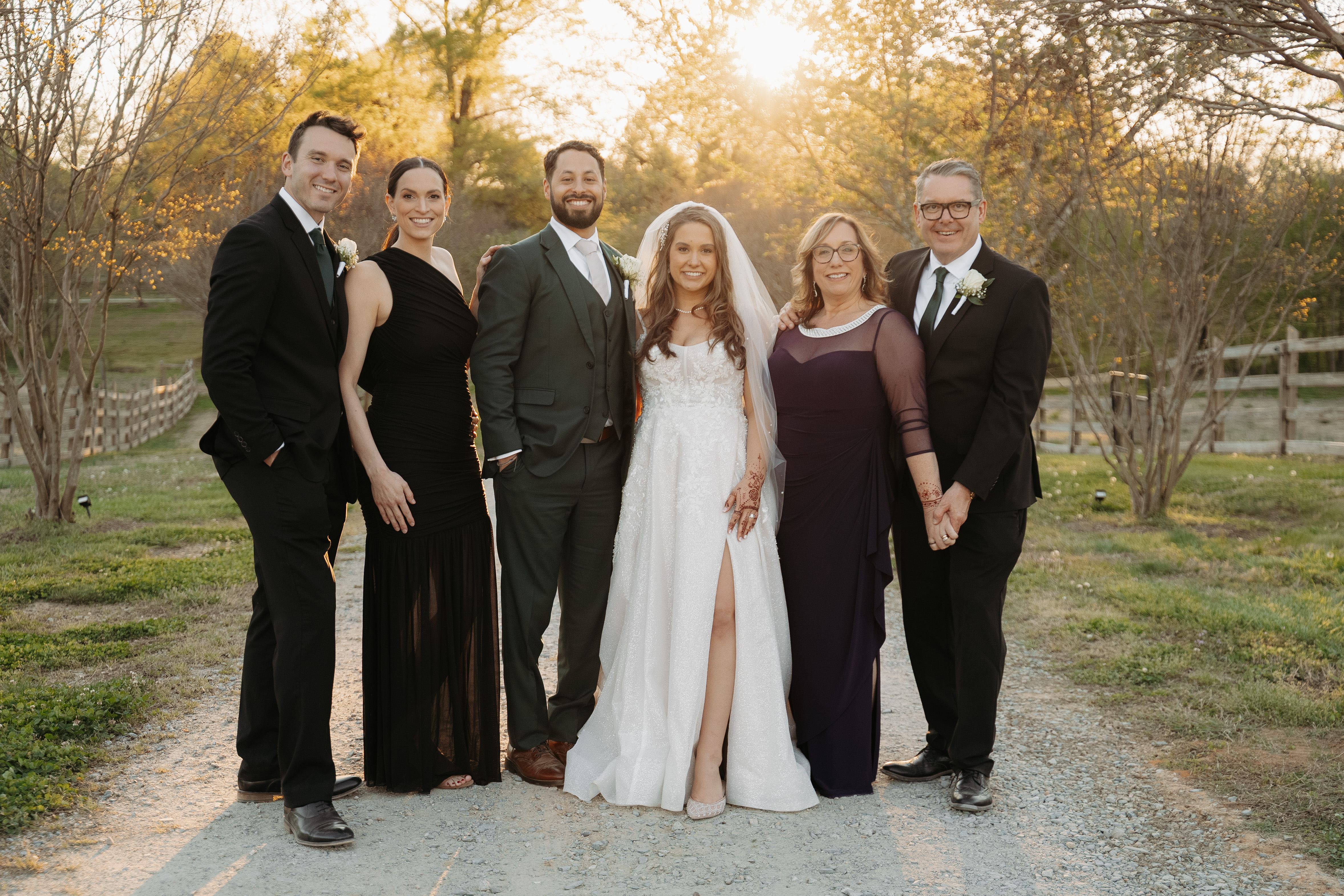 The full wedding party on a gravel drive in golden light