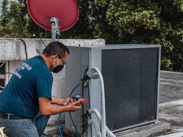 Technician checking refrigerant pressures on an AC condenser