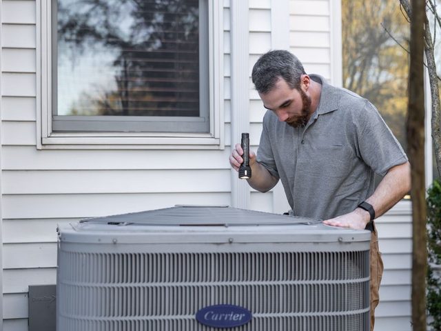 Technician inspecting an outdoor heat pump / condenser unit at a home